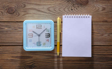 Alarm clock with notebook on wooden background. top viewの写真素材