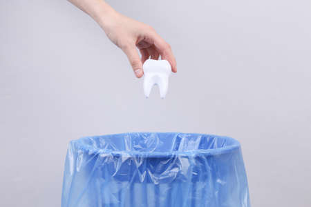 Hand throws plastic tooth into trash bin with package on gray backgroundの写真素材