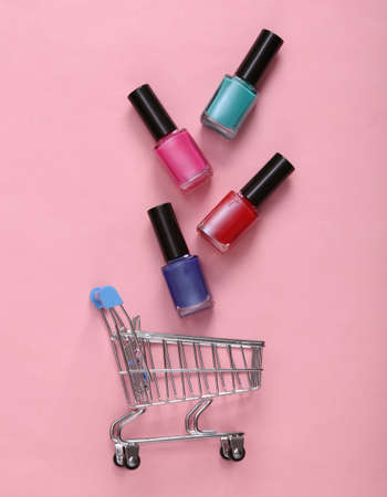 Nail polish bottles in shopping trolley on pink pastel background.の写真素材