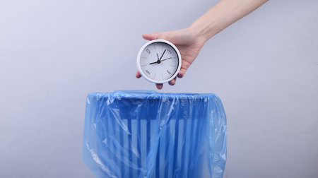 Hand throws clock into trash bin with package on gray backgroundの写真素材