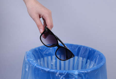 Hand throws sunglasses into trash bin with package on gray backgroundの写真素材