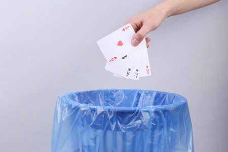 Hand throws four aces into trash bin with package on gray background