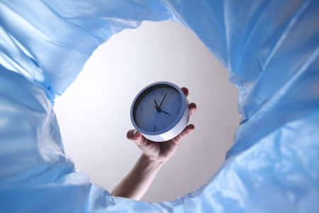 Bottom view hand throws clock into trash bin with blue bagの写真素材