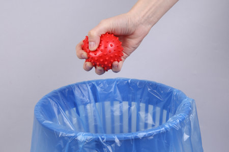 Hand throws virus strain model into trash bin with package on gray background