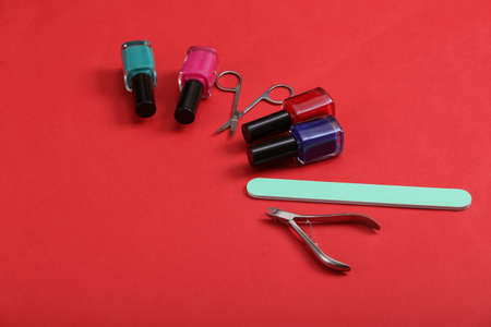 Manicure accessories. Nail polish bottles, scissors and nail file on red background.