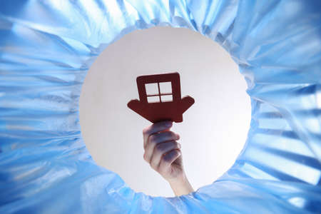 Hand throws house figure into trash bin with package. inside view