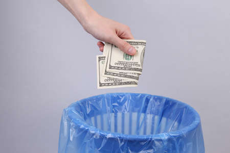 Hand throws dollar bills into trash bin with package on gray backgroundの写真素材