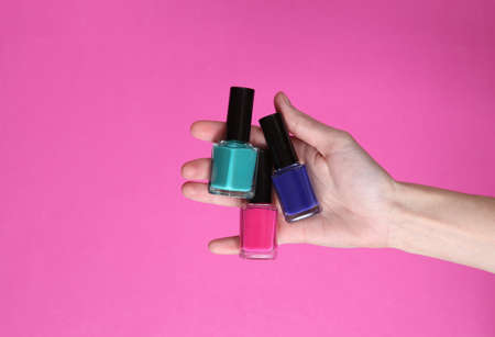 Female hand holding nail polishes on pink backgroundの写真素材