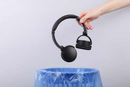 Hand throws plastic stereo headphones into trash bin with package on gray backgroundの写真素材