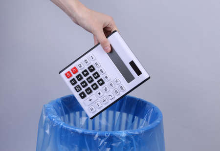 Hand throws calculator into trash bin with package on gray background