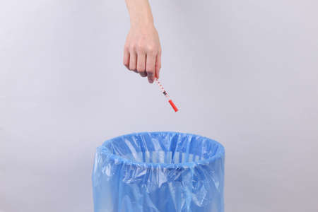 Hand throws syringe into trash bin with package on gray backgroundの写真素材