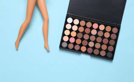Make-up palette of eye shadows and doll feet on a blue background. beauty still life.の写真素材