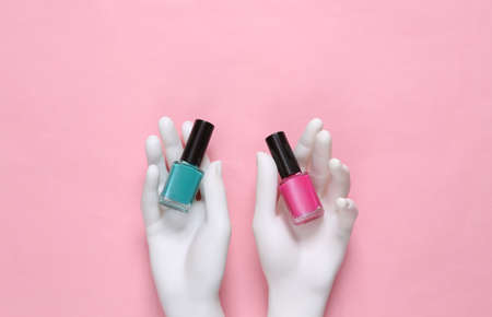 White mannequin hands holding bottles of nail polish on pink backgroundの写真素材