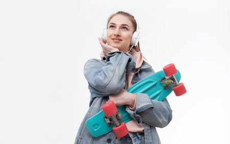 Young caucasian cheerful hipster woman in denim clothes with penny board and headphones listen music...