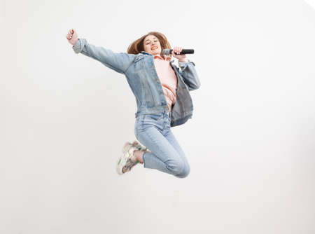 Cheerful energetic woman jumping with a microphone in her hands isolated on white background. I have...