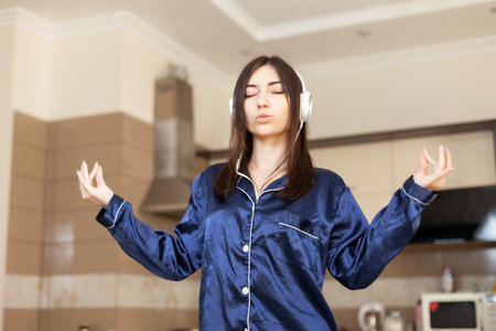 Meditating young woman in nightie and headphones in living roomの写真素材