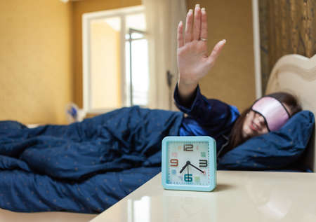 Young woman sleeping in bed. want to turn off alarm in dream. Ringing alarm clock. On table there is closeup alarm clockの写真素材