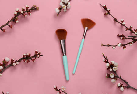 Makeup brushes and beautiful white flowering branches on pink background. Springtime beauty concept....