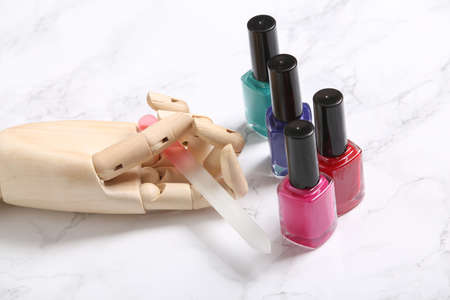 Wooden Mannequin hand holds nail file and bottles of nail polish on marble background. beauty layoutの写真素材