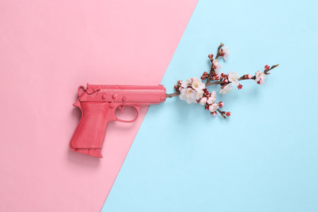 Pink gun with beautiful flowering branches on pink blue background. minimal concept. Flat lay, top...