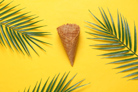 creative summer layout. Empty waffle cone with palm leaves on yellow background