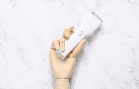 Wooden hand holding hair clipper on marble background