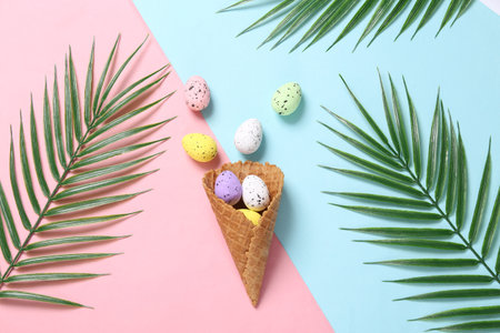 Colored eggs in waffle cone on pink blue background with palm leaves. creative easter layout