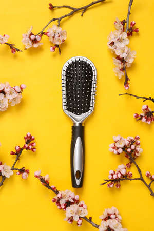 Hairbrush with beautiful white flowering branches on yellow background. springtime concept. Flat lay, top viewの写真素材