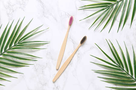 Eco bamboo toothbrushes with palm leaves on a marble background. Dental care concept