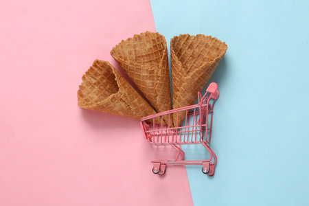 Mini shopping trolley with empty waffle cones on pink blue backgroundの写真素材