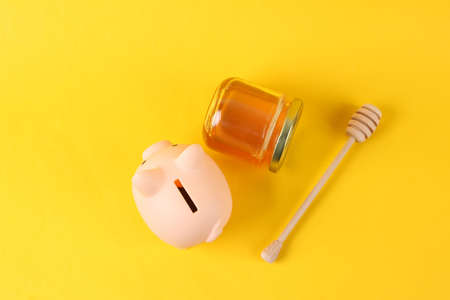 Piggy bank and Bee honey jar with honey wooden spoon on yellow backgroundの写真素材