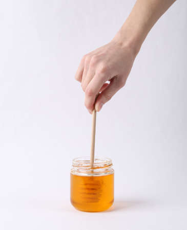 Hand holds honey spoon with jar of bee honey on white backgroundの写真素材