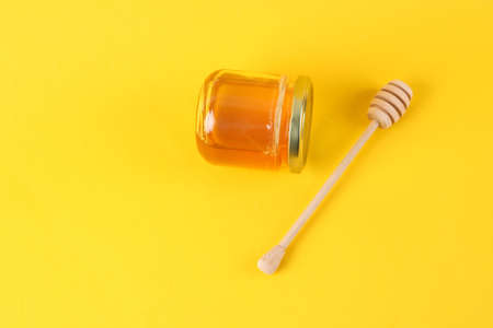 Bee honey jar and honey wooden spoon on yellow backgroundの写真素材
