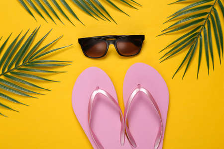 Flip-flops and sunglasses, palm green leaves on a yellow background. travel concept. tropical composition. top view. flat layの写真素材