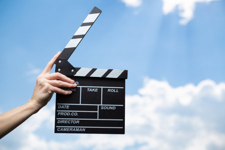 Hand holds movie board on background of blue sky with clouds.の写真素材