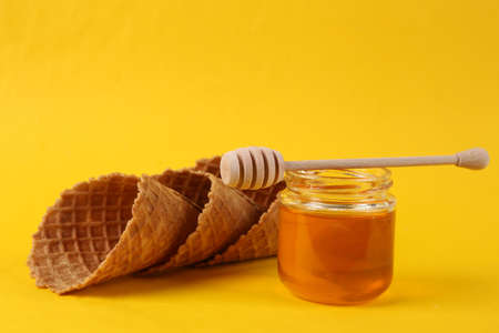 Jar of honey with waffle cones on yellow backgroundの写真素材