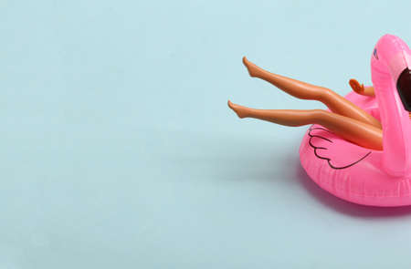 Doll resting on inflatable flamingos. Summer vacation, beach party. copy space