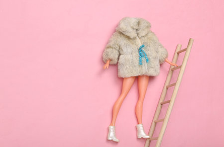 Doll in fur coat climbs the stairs up on a pink backgroundの写真素材