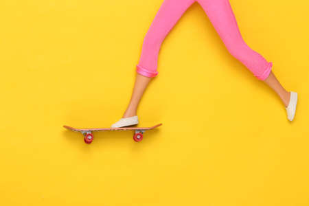 Doll legs ride on a skateboard on yellow background. minimalismの写真素材