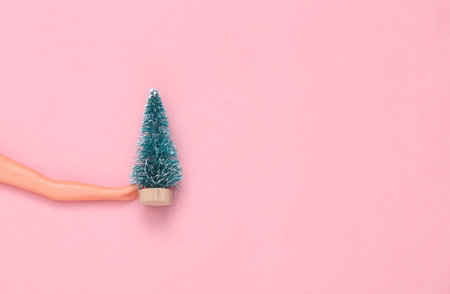 Doll hands holding Christmas tree on pink pastel background. Minmalism concept art.の写真素材