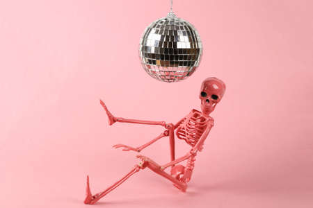 Disco ball and skeleton on pink background. Minimalism party concept