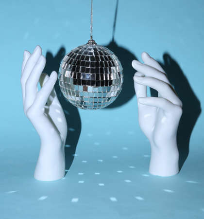 Disco ball with stand hands on blue background. Minimalist party concept