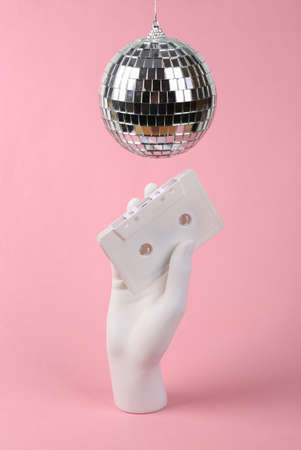 Disco ball and hand with audio cassette on pink background. Minimalism party concept