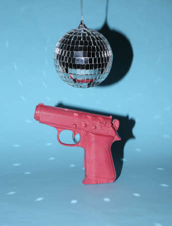 Disco ball and gun on blue bright background. Minimalism party concept