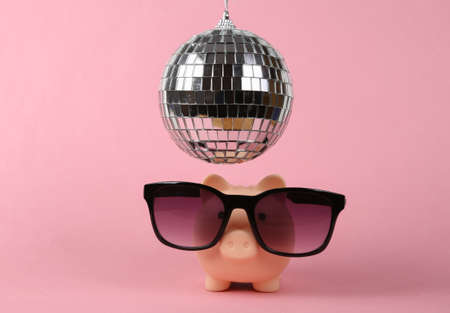 Piggy bank with sunglasses under disco ball on pink background. Minimalist party conceptの写真素材