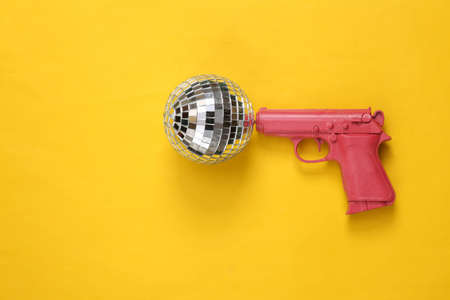 Disco ball with gun on yellow background. top view. flat lay. Minimalist party conceptの写真素材