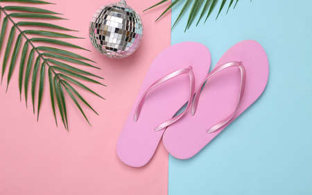 Disco ball with flip flops and palm leaves on a blue-pink background. top view. flat lay. Minimalism beach party and rest conceptの写真素材