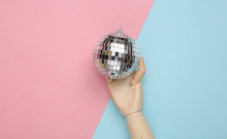 Wooden hand holding Disco ball on blue-pink pastel background. top view. flat lay. Minimalist party conceptの写真素材