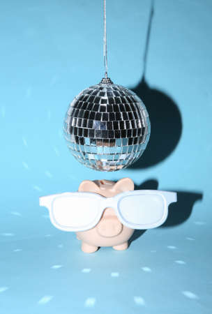 Piggy bank with glasses under disco ball on blue bright background. Minimalist party concept