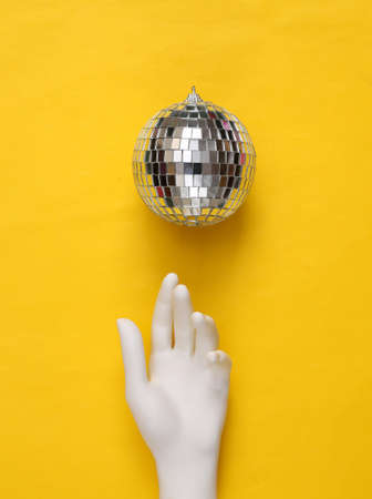 Disco ball and hand on yellow background. Minimalist party concept